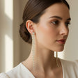 Pair of long, thin chain earrings with clear stones worn by a woman on a neutral background