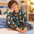 Boy in a charcoal grey PJ set with colourful dinosaur print, sitting on a bed with a blue blanket