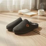 Pair of charcoal felt mule slippers on a wood floor showing the small leather crest