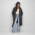 Charcoal long knit cardigan with the hood up, hands in the front pockets