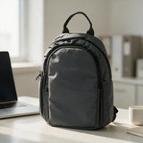 Charcoal mini backpack with a top handle and zip front pocket on an office desk beside a laptop