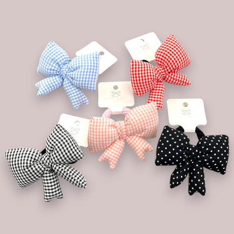Six gingham and polka dot fabric bow hair ties arranged on a mauve background