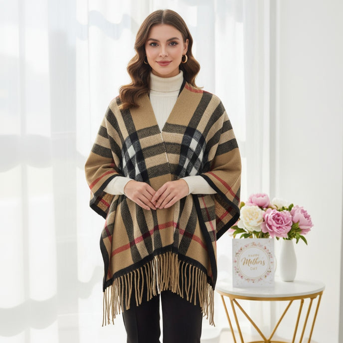 Woman wearing a plaid puncho with fringe, standing in a bright room with a decorative table and flowers