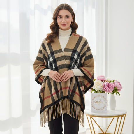 Woman wearing a plaid puncho with fringe, standing in a bright room with a decorative table and flowers