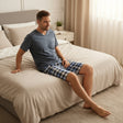 Checkered short pyjama set worn seated on the edge of a made bed