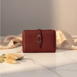 Red wallet with a gold buckle on a marble surface with beige fabric