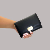 Black wallet held by a hand with light pink nail polish on a grey background