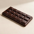 Dark brown chocolate bar squishy with raised glossy squares on a beige surface
