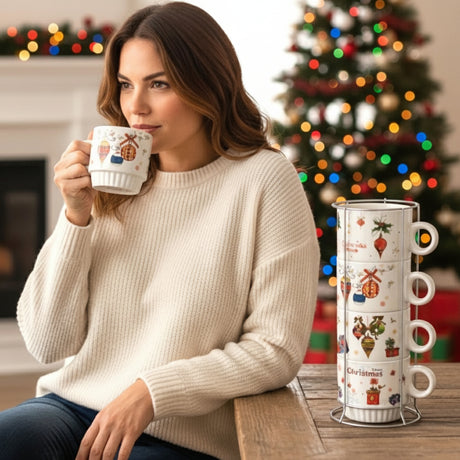 Woman sipping from a festive ornament mug with the stacked set beside a Christmas tree