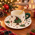 White ceramic teacup with a Christmas tree print, green handle, printed saucer and reindeer spoon