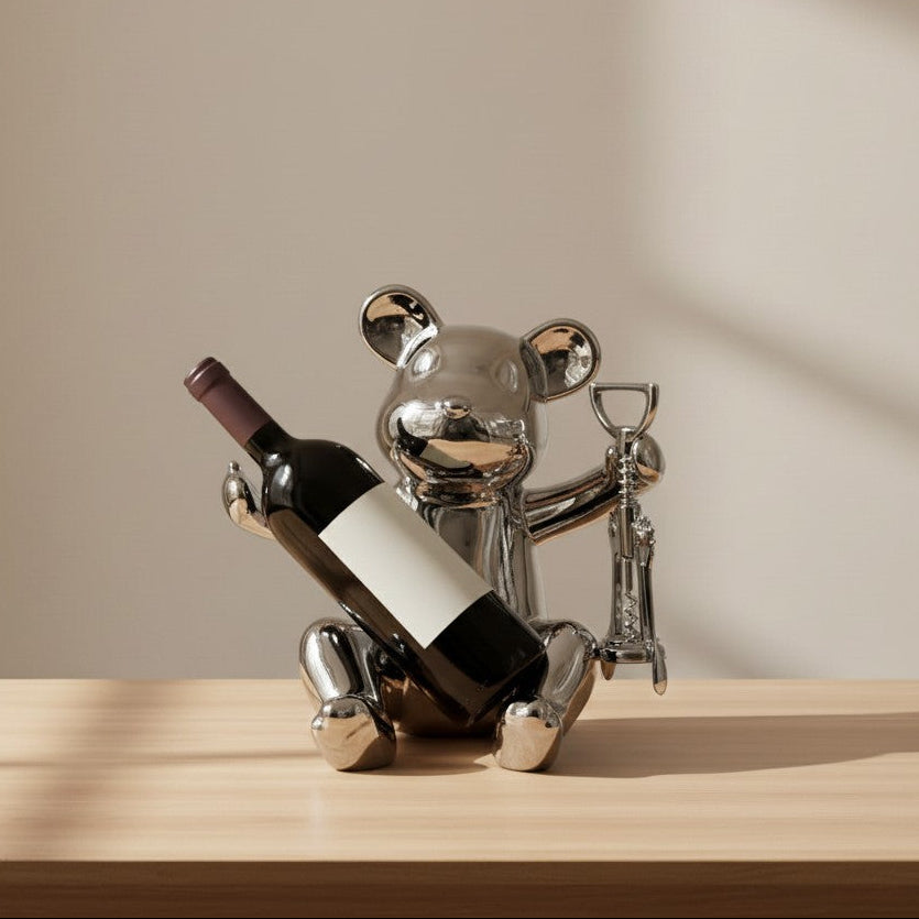 Metallic bear-shaped wine bottle holder with a bottle on a wooden surface and beige background