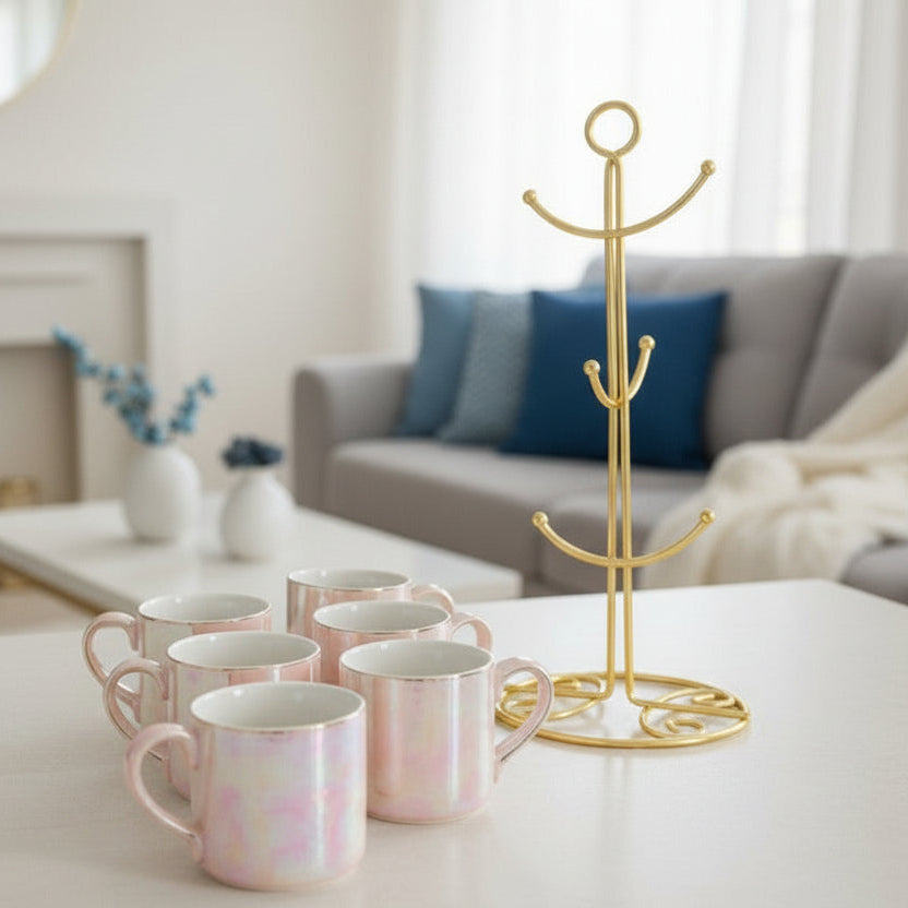 Six blush pink pearlescent ceramic mugs beside an empty gold mug stand