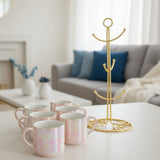 Six blush pink pearlescent ceramic mugs beside an empty gold mug stand