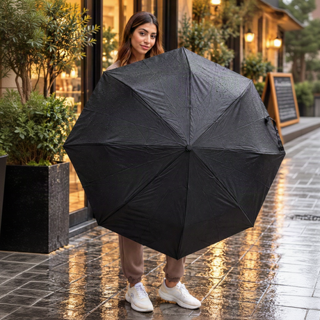 Woman holding open a plain black folding umbrella beaded with raindrops