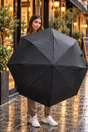 Woman holding open a plain black folding umbrella beaded with raindrops