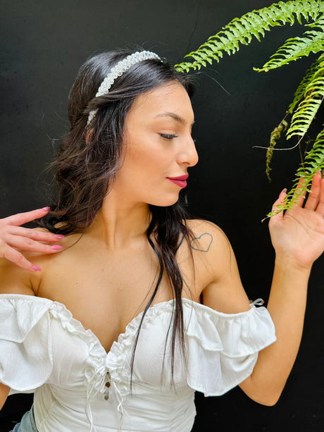 Woman in a white off-shoulder top wearing a crystal tiara against a black background