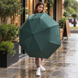 Woman holding open a plain forest green folding umbrella on a wet street