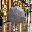 Woman on a rainy street holding open a plain grey folding umbrella
