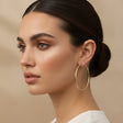 Gold hoop earrings worn by a woman on a beige background