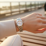 Silver watch with pale dial worn on the wrist at sunset