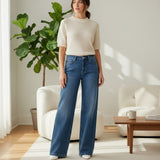 Woman wearing a white sweater and blue wide jeans standing in a bright living room