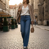 Woman walking down a street wearing a beige blazer, white shirt, blue wide jeans, and holding a brown handbag