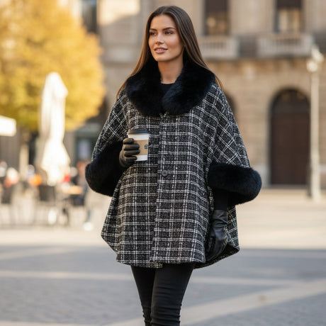 Woman in a checkered puncho with black fur trim holding a coffee cup on a city street