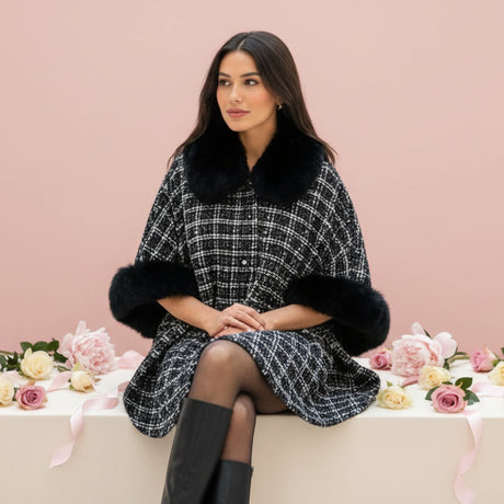 Woman wearing a black and white checkered puncho with black fur trim sitting on a pink couch with flowers