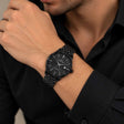Black steel watch with date window and link bracelet worn with a black shirt