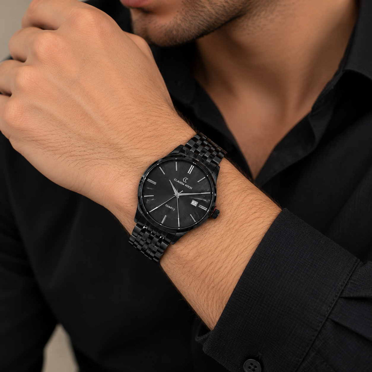 Black steel watch with date window and link bracelet worn with a black shirt