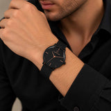 Minimal black mesh strap watch with rose gold hands worn on a man's wrist