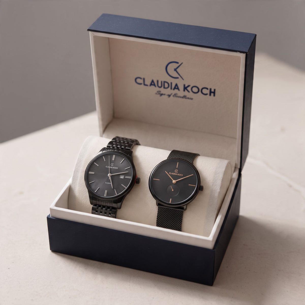 Two black men's watches, one on a link bracelet and one on a mesh strap, in an open gift box