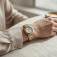 Gold watch with white dial and ridged bezel worn with a cream blouse at a table