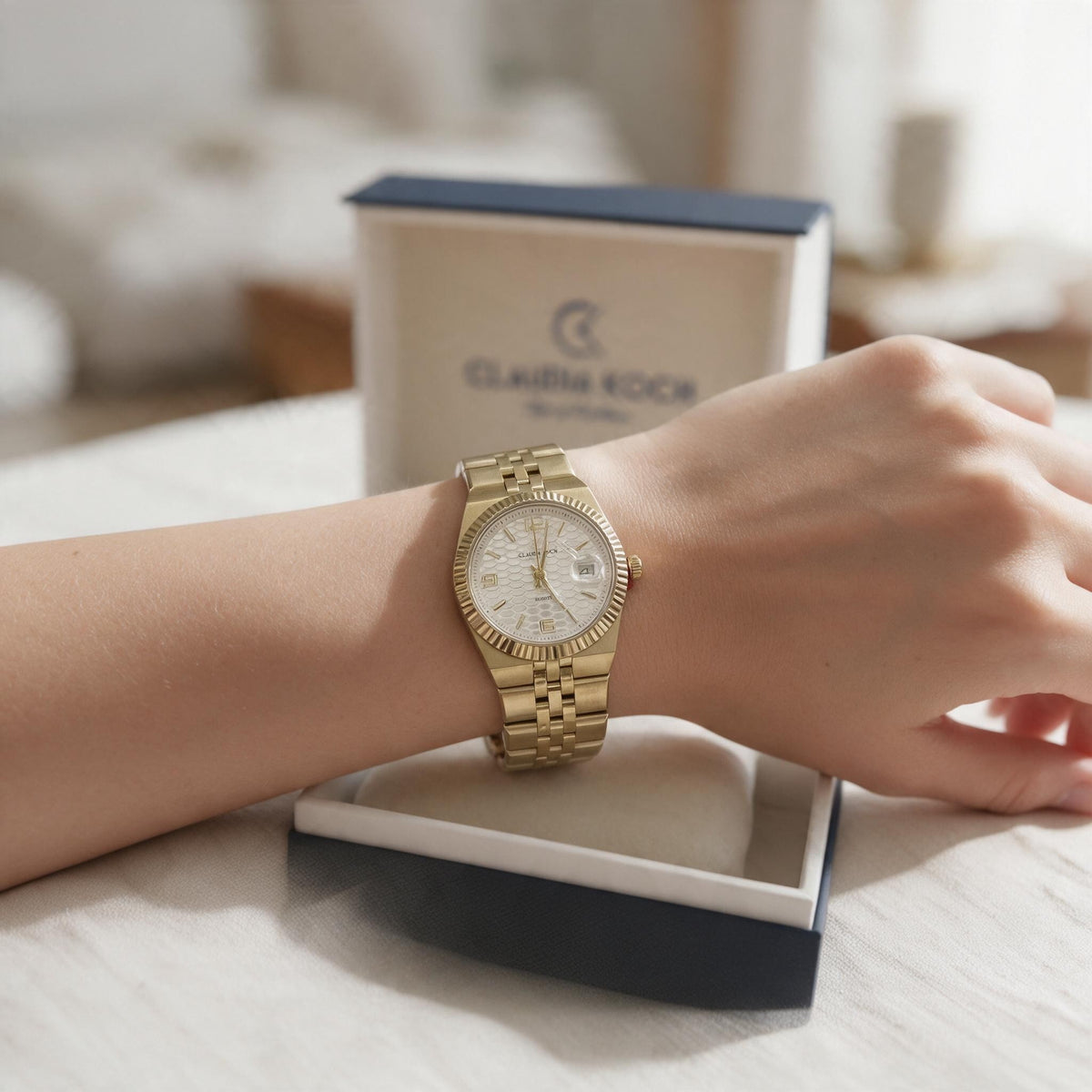 Gold fluted bezel watch with textured white dial worn in front of its box