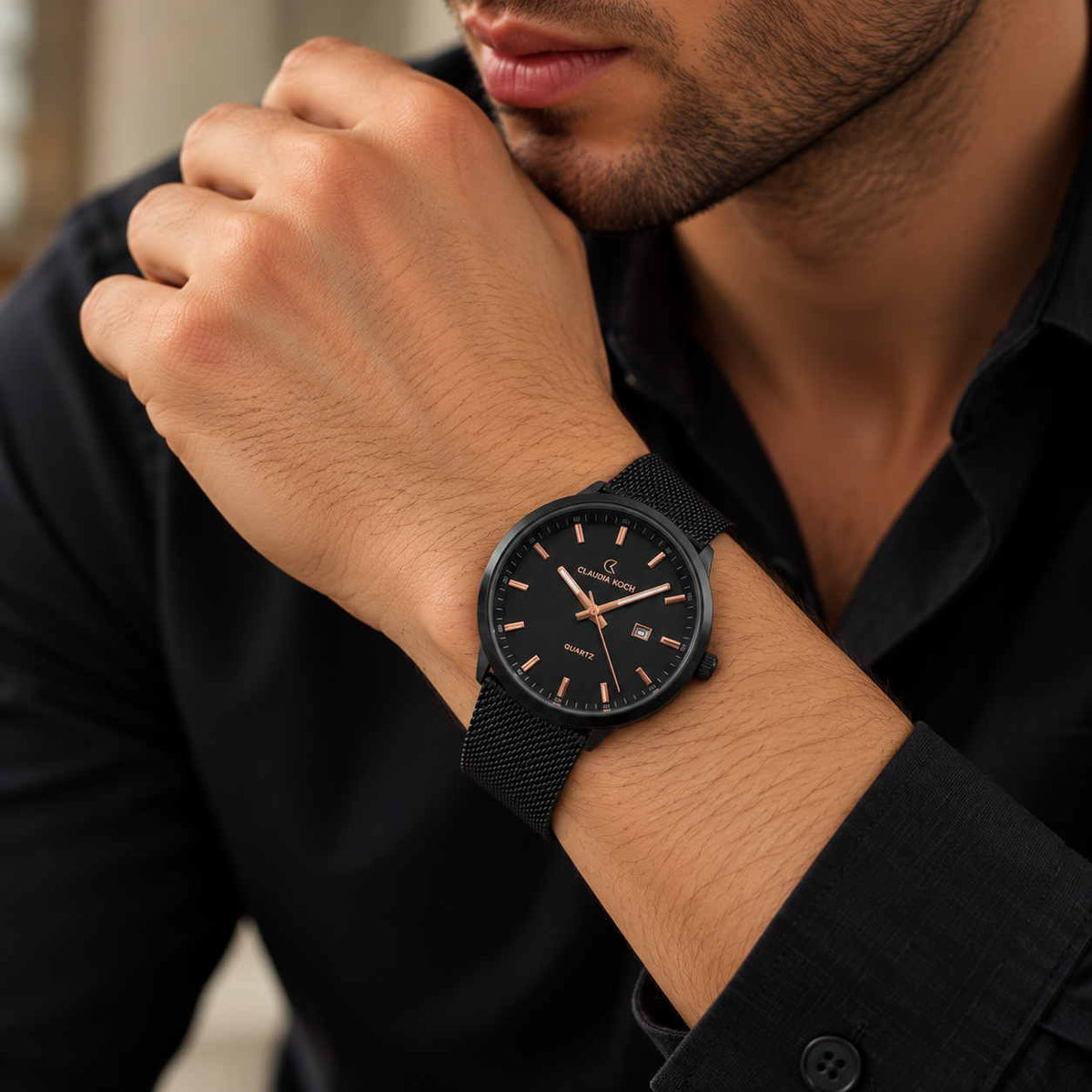 Black mesh strap watch with rose gold markers and date window worn with a black shirt