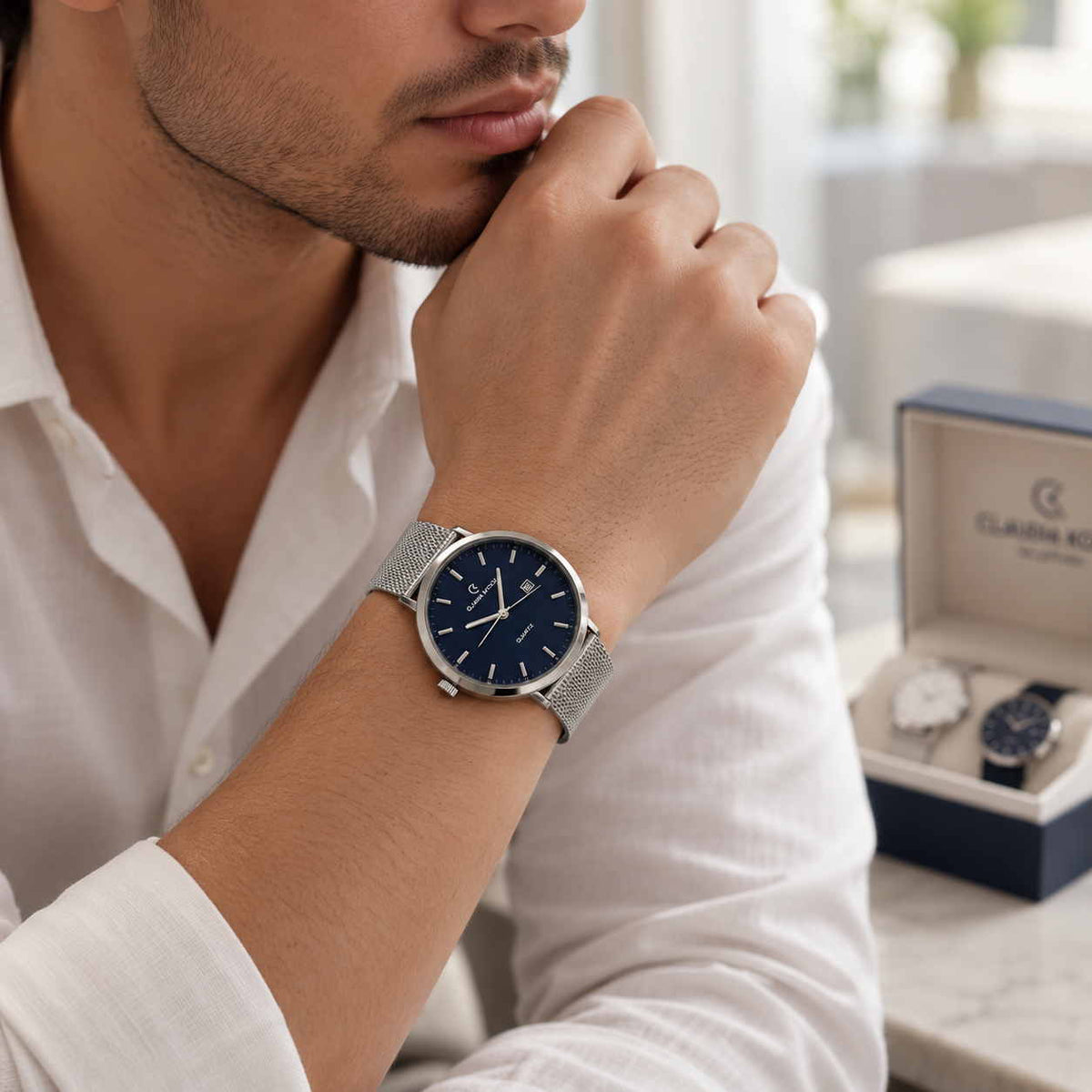 Silver mesh strap watch with navy dial worn with a white shirt beside an open gift box