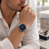 Silver mesh strap watch with navy dial worn with a white shirt beside an open gift box