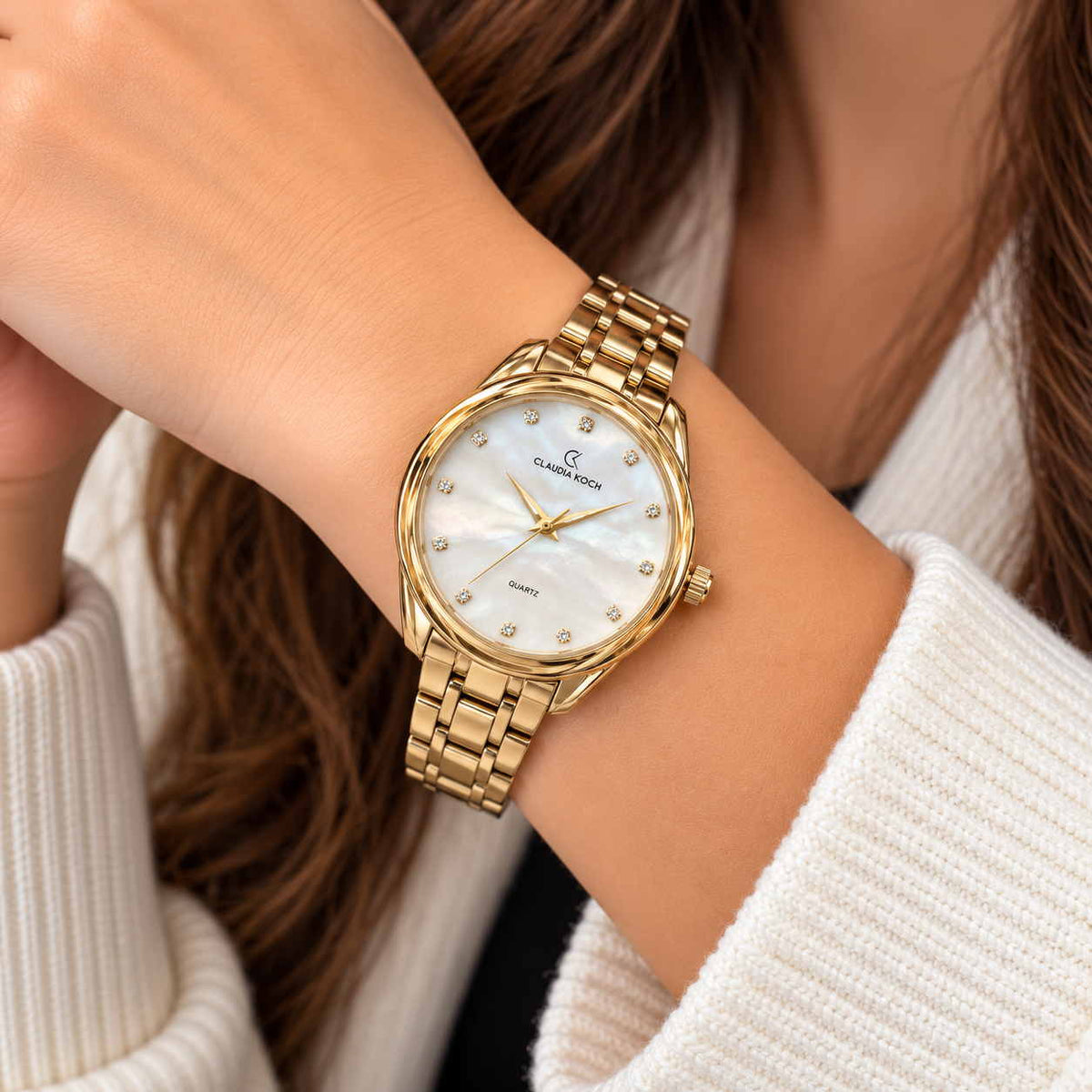 Gold watch with white pearl dial and crystal markers worn on the wrist