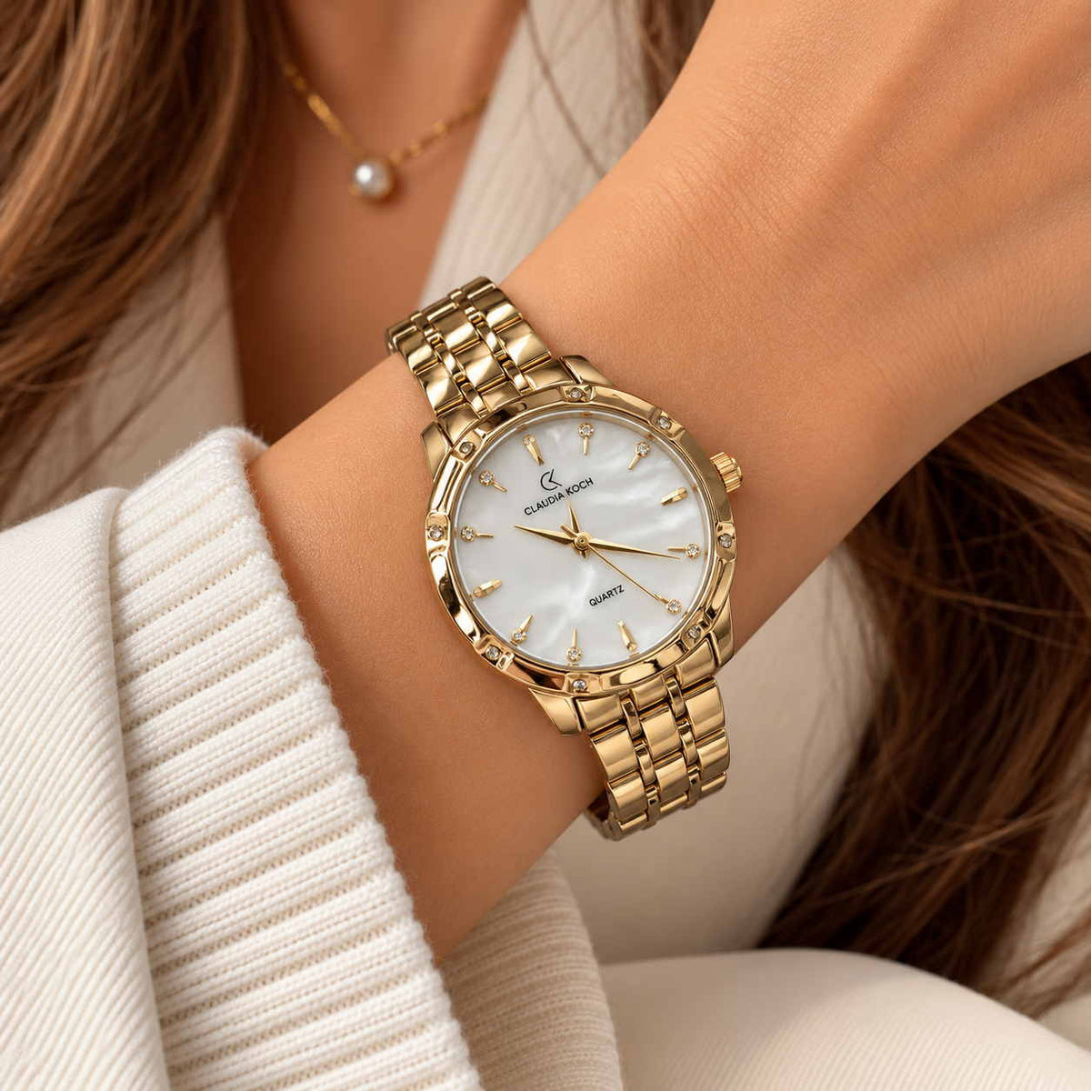 Gold watch with white pearl dial and faceted bezel worn beside a pearl necklace