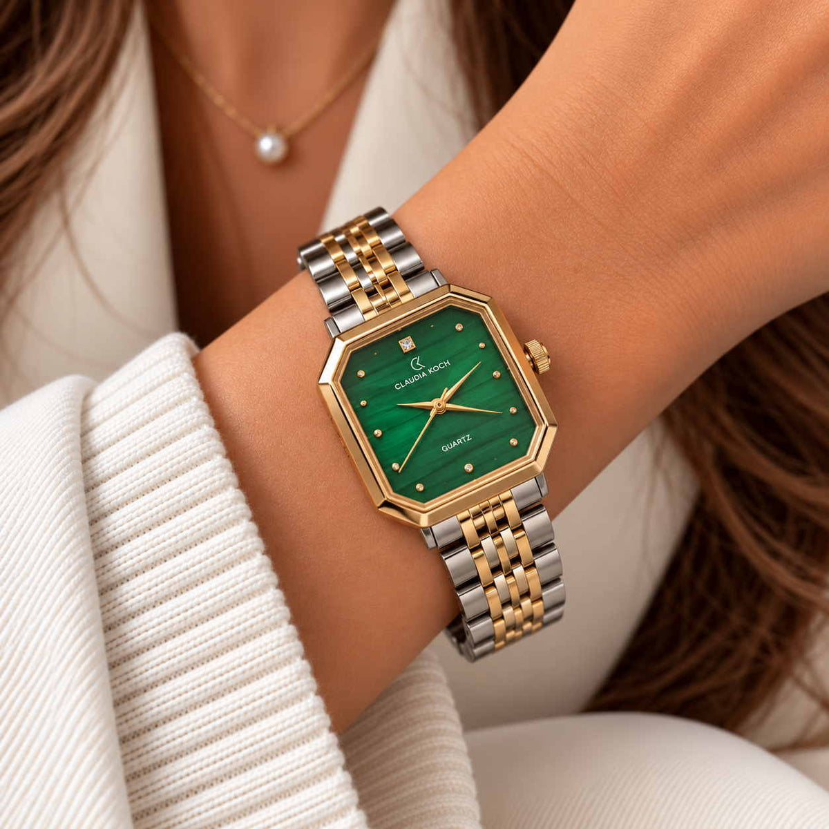 Two tone rectangle watch with emerald green dial worn with a pearl necklace