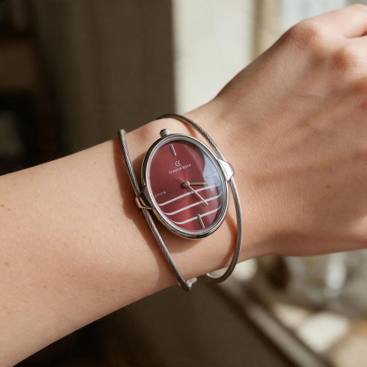 Red oval dial bangle watch with double silver wire cuff worn on the wrist