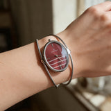 Red oval dial bangle watch with double silver wire cuff worn on the wrist