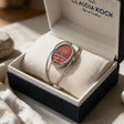 Red oval dial bangle watch with open silver wire cuff resting in a gift box