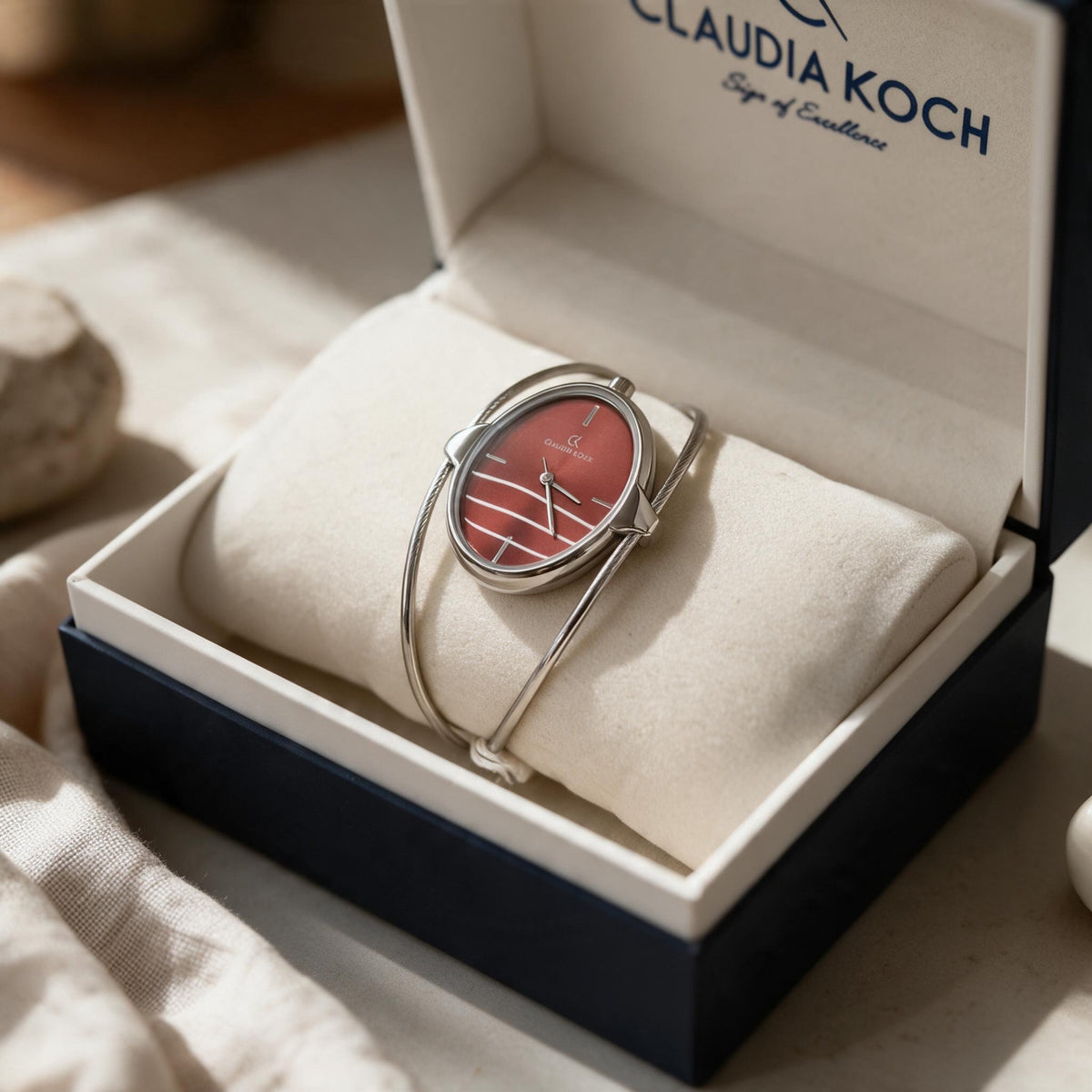 Red oval dial bangle watch with open silver wire cuff resting in a gift box