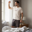 Man wearing a cream coffee print tee and grey shorts by a sunlit window