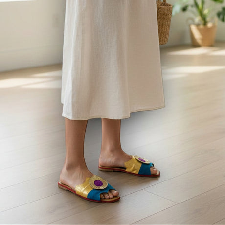 Person wearing a white dress and colorful handmade sandals in a bright room with plants