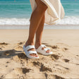 Woman wearing a pair of white sandals on sand