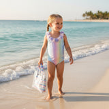 Young girl in a colorful swimsuit standing on a beach with ocean waves.
