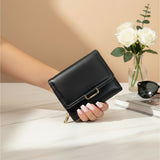 Black wallet held by a hand on a desk with a laptop and flowers in the background