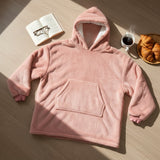 Dusty pink hooded blanket in plush fleece laid flat beside a book and coffee